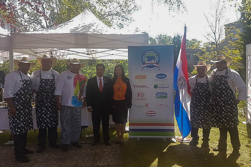 El embajador Fernando Ojeda Caceres y señora, junto al equipo de Asado Benítez posando ante el banner donde se promociona las marcas de carne paraguaya.