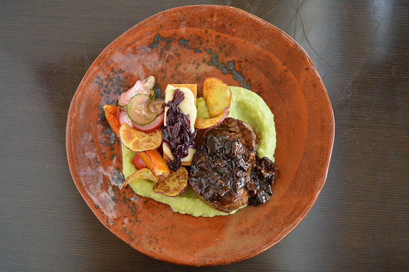 Lomito en corte churrasco, con sopa paraguaya con queso de cabra, acompañado de verduras de estación en diferentes texturas, cebolla caramelizada, y una salsa de shiitakes, caña y miel.