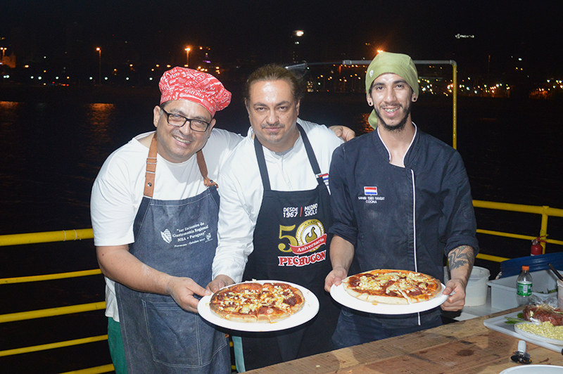Agostino, Vidal y Mauricio, los encargados de la preparación de las pizzas. Sobre el fondo negro de la Bahía de Asunción, se recortan las luces de los edificios del centro de la ciudad.
