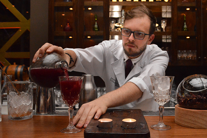 El bartender vestido con guardapolvo blanco, preparando el Blood Bank, que lleva vodka, oporto, jengibre, naranja, y biter Angostura. 