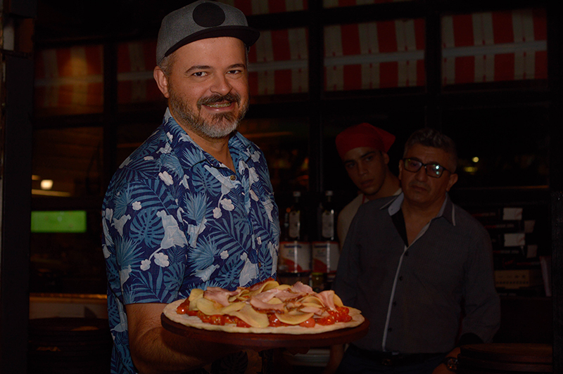 El Gordo exhibiendo su pizza de otoño. Pueden verse las láminas de papa, los tomates casi enteros a poco de entrar al horno.