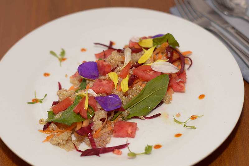 Ensalada de quinoa, remolacha, zanahoria, rúcula, tomates, vinagreta de naranja decorado con pétalos de flores comestibles.