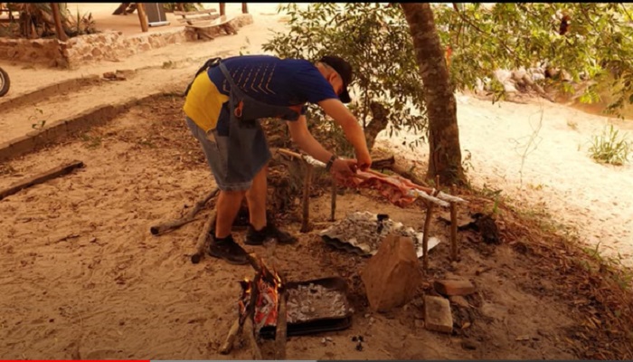 Antoliano Acosta, parrillero del equipo Adela Memby preparando el asado en la improvisada parrilla, recurriendo a palos de escoba y alambre, en la playa, al costado del arroyo.